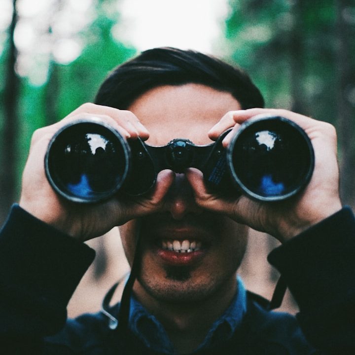 Fernglas Mann mit Fernglas in der Natur, lächelt in die Kamera.